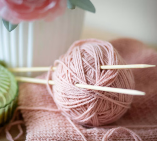 a pink ball of yarn and knitting needles