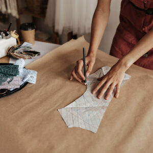tanned woman in linen red dress draws cloth pattern on craft paper. fashion designer creates garmen